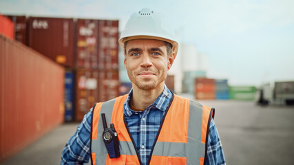 Smiling Portrait of a Handsome Caucasian Industrial Engineer in White Hard Hat, Orange High-Visibility Vest, Checkered Shirt and Work Gloves. Foreman or Supervisor Stanging in Container Terminal. - Powered by Adobe