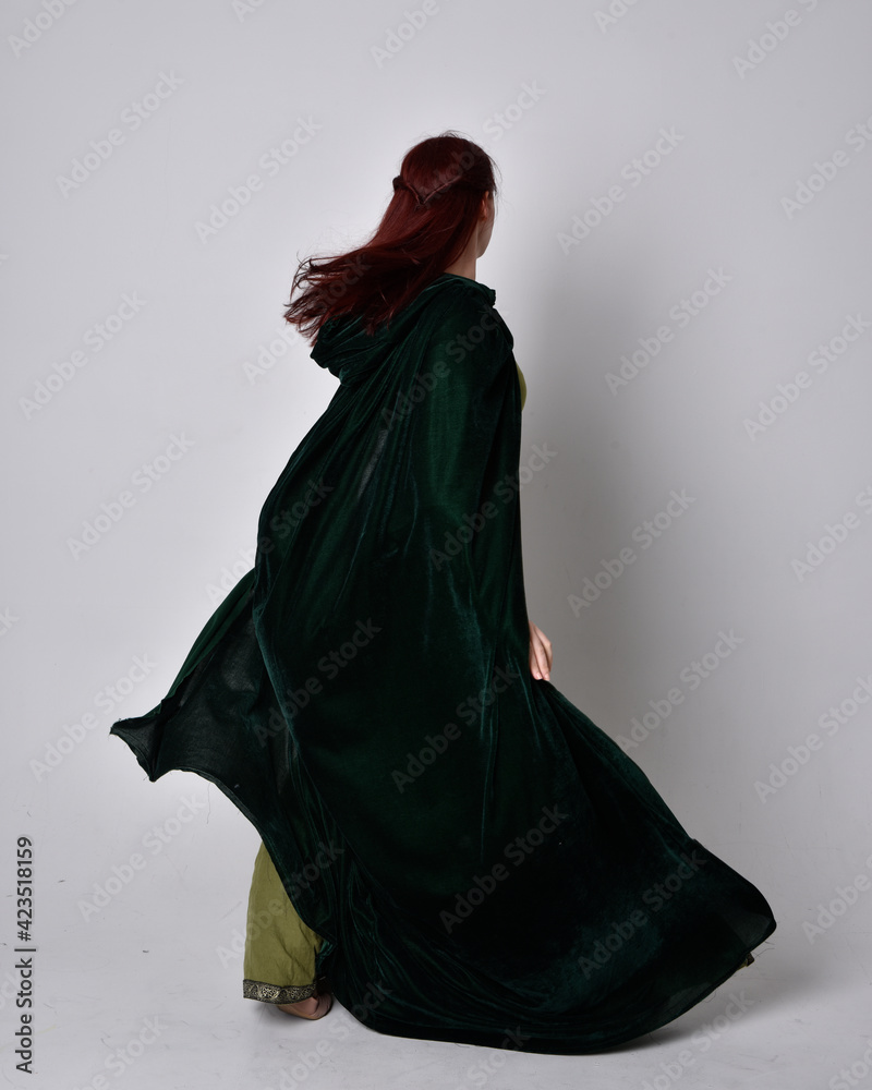 Sticker full length portrait of red haired girl wearing celtic, green medieval gown with fantasy velvet cloak. Standing pose isolated against a studio background.