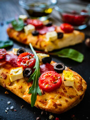 Focaccia - roasted mozzarella sandwiches with salami pepperoni, feta cheese and tomatoes on black stone plate 