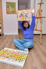 Young woman showing her palette and painting on canvas with oil paints at home. Artist drawing on the floor.