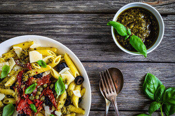 Penne with basil pesto, parmesan, black olives and sun-dried tomatoes on wooden table 