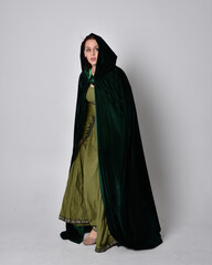 full length portrait of red haired girl wearing celtic, green medieval gown with fantasy velvet cloak. Standing pose isolated against a studio background.