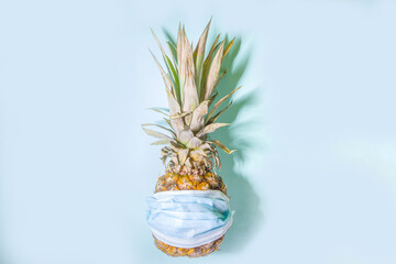Pandemic summer vacation 2021. Tropical fruits, ripe pineapple with medical mask, holiday in new-normal covid-2019 world concept , with hard light on blue modern background