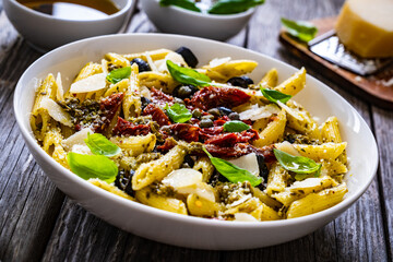 Penne with basil pesto, parmesan, black olives and sun-dried tomatoes on wooden table 