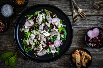 Marinated herrings with roasted beetroots and fresh vegetable leaves on wooden table
