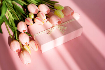 Bouquet of tender tulips and gift box isolated on pink background with shadow. Spring flowers. Greeting card for Birthday, Woman, Mother's Day, Wedding, Valentine's day. Flat lay. Copy space