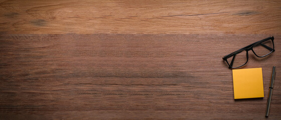 Top view of eyeglasess, sticky notes and pen over wooden table with copy space