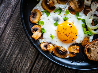 Continental breakfast - sunny side up eggs on white mushrooms, onion and greek salad on wooden table