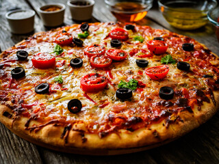 Pizza with ham, tomatoes, olives, parmesan and mozzarella on wooden background
