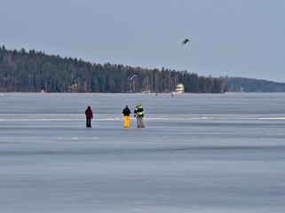 People enjoying on sunshine and watching kite surfers on lake ice in spring