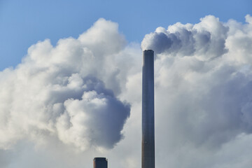 Close-up view of CHP plant pipes with smoke in the sunny day.