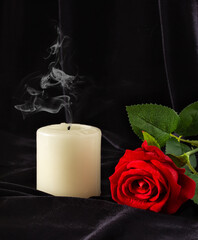 An extinguished candle and a red rose on a black background. The concept of mourning, condolences, funerals.