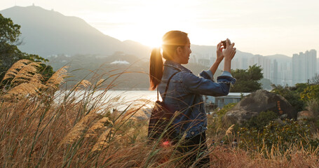 Woman uses mobile phone to take photos at sunset