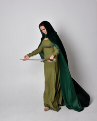 full length portrait of red haired girl wearing celtic, green medieval gown with fantasy velvet cloak. Standing pose isolated against a studio background.