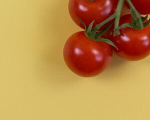 branch of small red tomatoes on yellow background. flat lay 