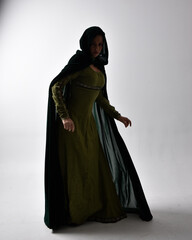 Naklejka premium full length portrait of red haired girl wearing celtic, green medieval gown and velvet cloak with shadowy backlighting. Standing pose isolated against a studio background.
