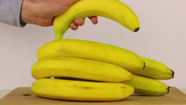 Woman's hand picks fresh bananas from the heap. Close-up video. Healthy food concept.