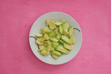 Avocat coupé en morceaux dans une assiette sur fond rose. Vue du dessus