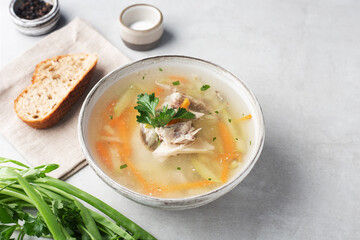 chicken soup in a bowl on a gray table with herbs and spices, a piece of bread
