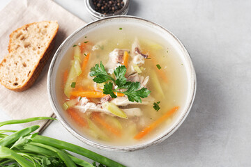chicken soup in a bowl on a gray table with herbs and spices, a piece of bread, top view