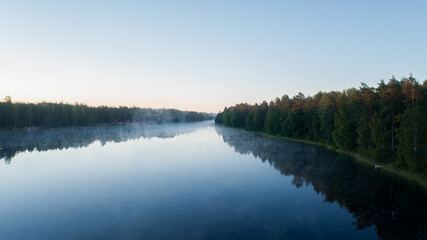 Aerial view of foggy lake at sunrise in summer. Colorful landscape with forest in low clouds, lake, meadow in fog, clear sky