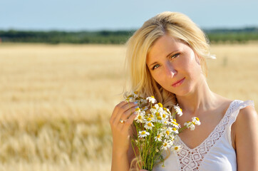 Happy woman posing with camomile in golden wheat.