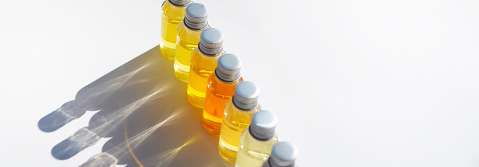 Vials of colored liquid are arranged in a row. Curly shadows fall on a white background.
