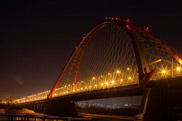 Fototapeta na wymiar night view of the bridge over the river, the lanterns of which brightly illuminate everything around 