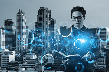 Eastern young businessman looking into his notebook to achieve tremendous growth in business based on technologies. Worldwide process to conduct transactions. Tech hologram icons over Bangkok