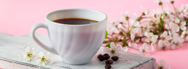 Strong espresso coffee on a white wooden tray. Spring flowers of an apple tree on a pink background. Good morning and spring time concept.