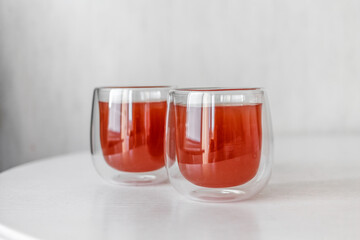 Red drink in elegant glass on white table. Two Bright juice in light background. Compote natural refreshment in empty surface. Clean horizontal concept