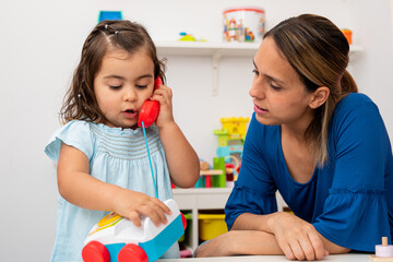 Little girl and her kindergarten teacher play with a toy phone, pretending to have conversations.