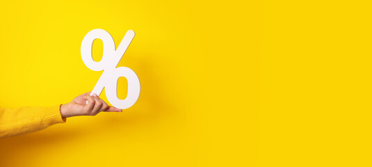 hand holding percentage sign over yellow background, panoramic image