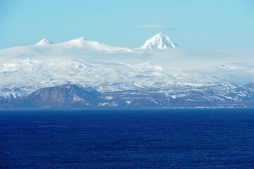 Fototapeta na wymiar Mountains covered with snow in Aleutian Islands as a part of island chain in Alaska observed form container vessel sailing over Pacific ocean during sunny winter weather and calm sea.