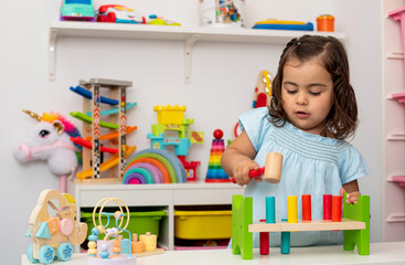 Two-year-old girl of Caucasian origin, playing with a hammer in kindergarten.