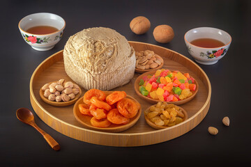 Sunflower halva sprinkled on a wooden platter with pistachios, peanuts, dried apricots, candied fruit syrup and Asian tea cups on a dark background. Eastern sweets.