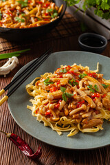 Traditional noodles with shimeji mushrooms and chicken. Prepared in a wok. Served on a gray plate.