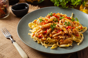 Traditional noodles with shimeji mushrooms and chicken. Prepared in a wok. Served on a gray plate.