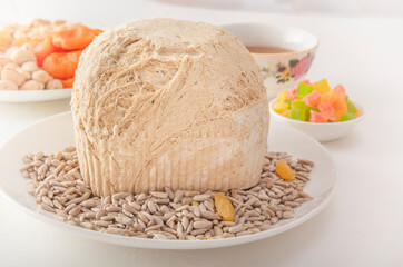 Sunflower halva on a white plate against the background of pistachios, peanuts, candied fruits, raisins, dried apricots and Asian cups for tea on a white table. Eastern sweets. Close-up
