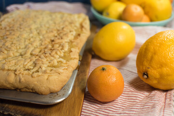 Naklejka na ściany i meble a delicious lemon shortbread pie on a metal baking sheet and wooden board sits on a striped towel with ripe yellow and orange citrus fruits
