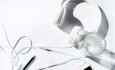 White background. Border from white headphones of a smartphone with a glass of water and a black pencil. Copy space for text.