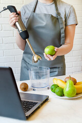 girl in an apron holds a mixer and an apple. making fruit smoothies according to a recipe from the Internet