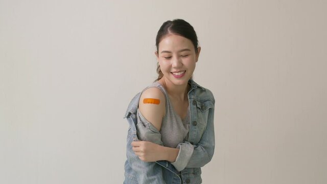 Young attractive beautiful asia female or teenage receive covid-19 anti virus vaccine in campaign vaccination safe life happy smile cheerful with blue, yellow, pink bandage on arm with copy space.
