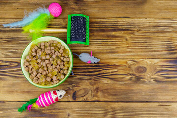 Fototapeta na wymiar Canned cat food in bowl, cat toys and pet slicker brush on wooden background. Top view, copy space. Pet care concept