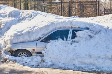 The old broken car is completely covered with snow.