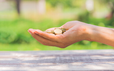 money saving and business financial concept. business man holding golden coin money in hand in the park outdoor against green blur nature background.
