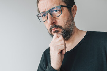 Fototapeta premium Portrait of mid-adult contemplative man with eyeglasses, man thinking and holding chin