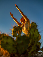 Asian girl doing yoga with arms outstretched in an outdoor landscape with prickly pears at sunset