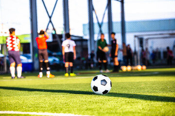 Obraz premium Soccer ball on green artificial turf with blurry coach and soccer team are training. Blurry kid soccer players training in soccer academy.