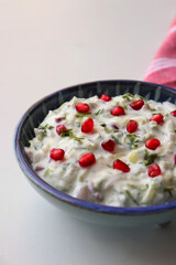 Pomegranate and Cucumber Raita. Indian Fresh sauce or condiment called Raita. Yogurt mixed with grated cucumber, onions,  pomegranate, and spices. Garnished with fresh coriander. Copy space.